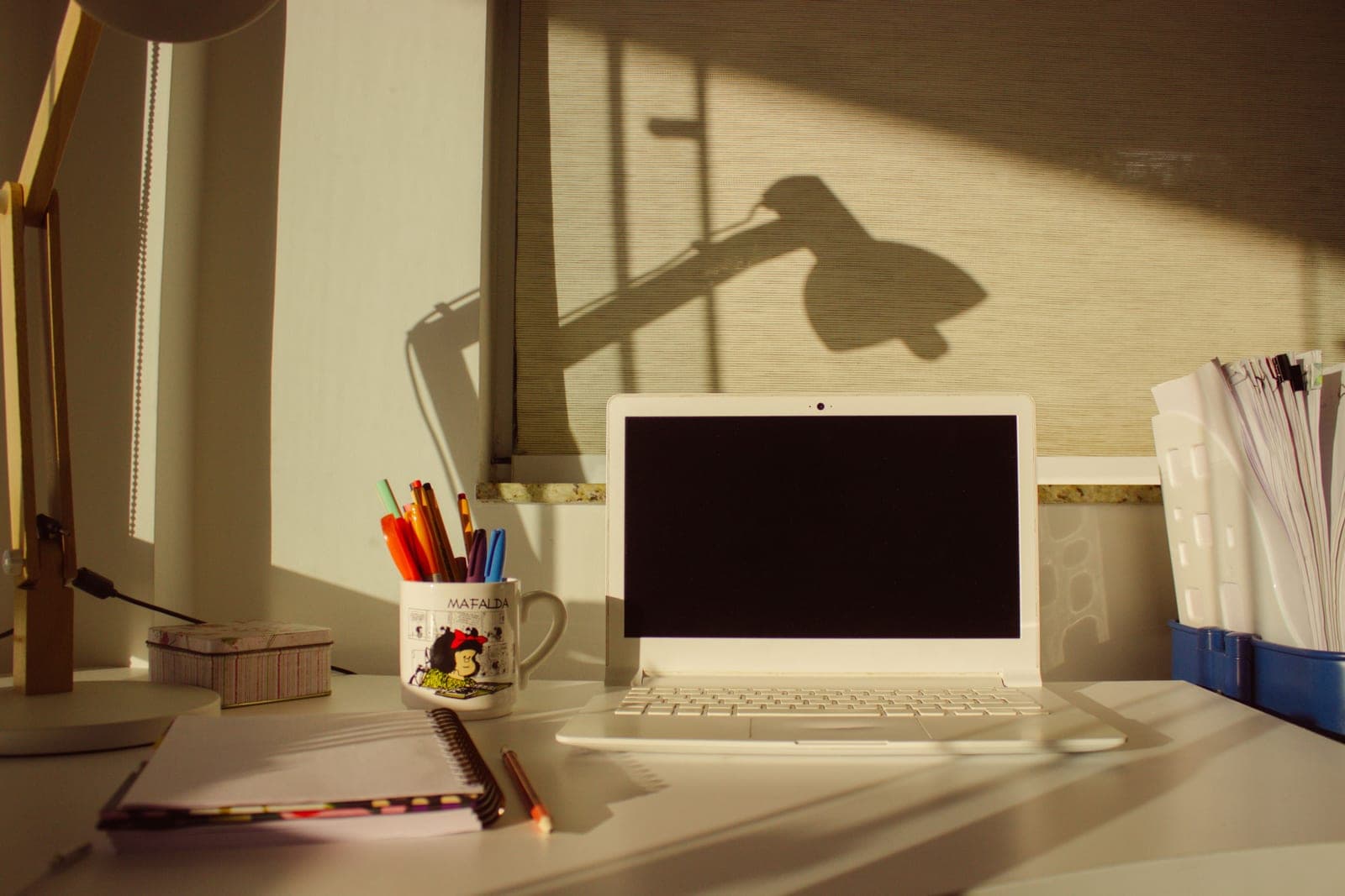 A writing desk with a notebook, a lamp and a mug in warm evening light