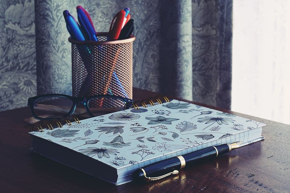A mesh pen cup, spiral notebook and fountain pen on a wooden desk
