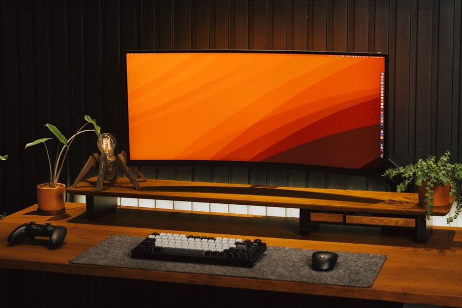 A wide desk with a curved monitor, plants and tech accessories