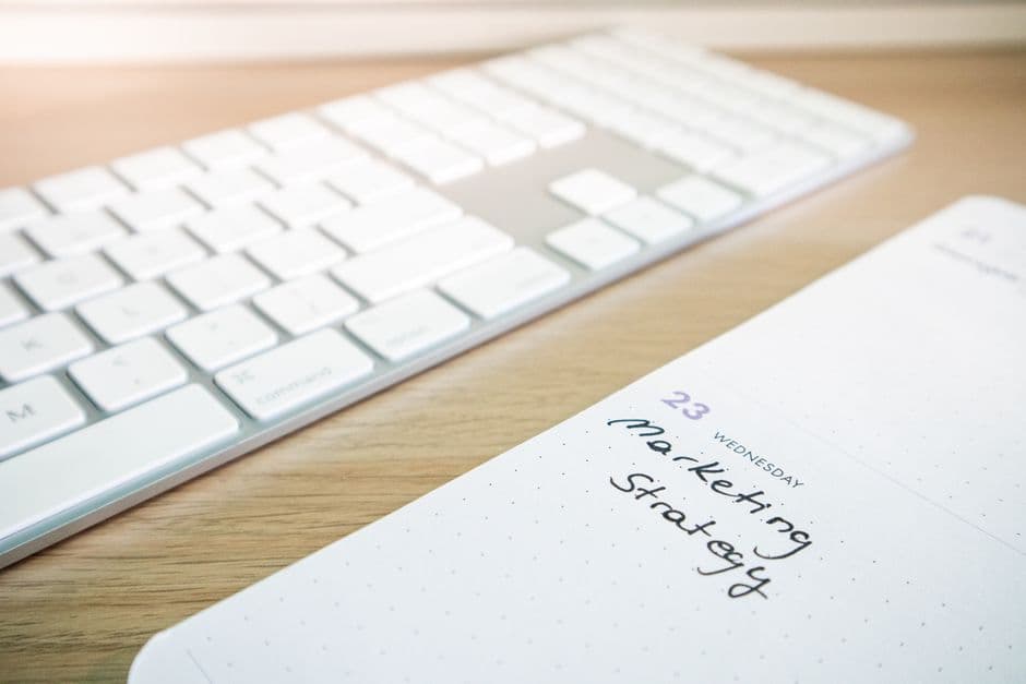 A keyboard and an open planner side by side on a wooden office desk
