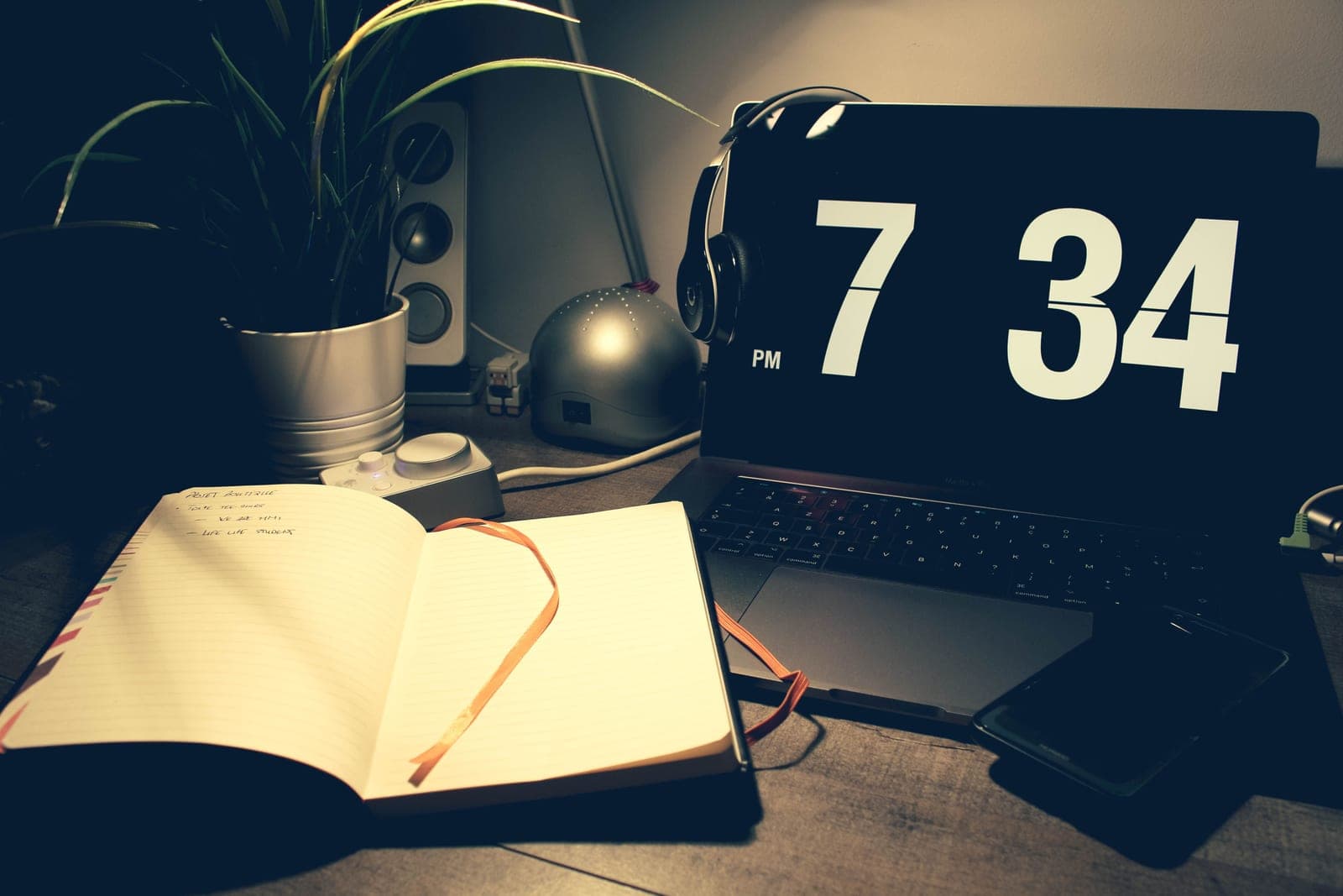 A minimal warm desk setup with a lamp, notebook and plant