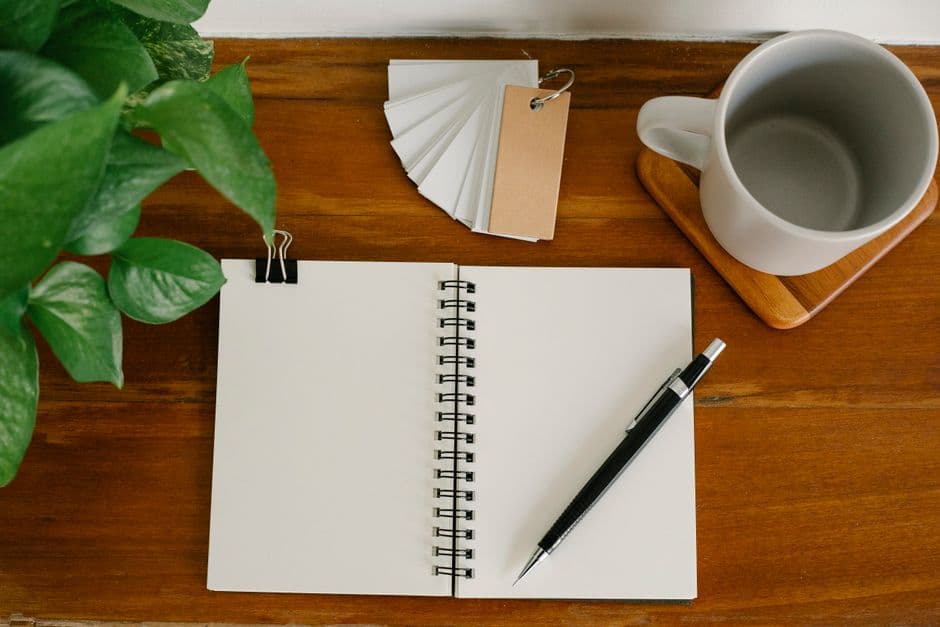 A wooden desk from above with a notebook, pen, mug and a small potted plant