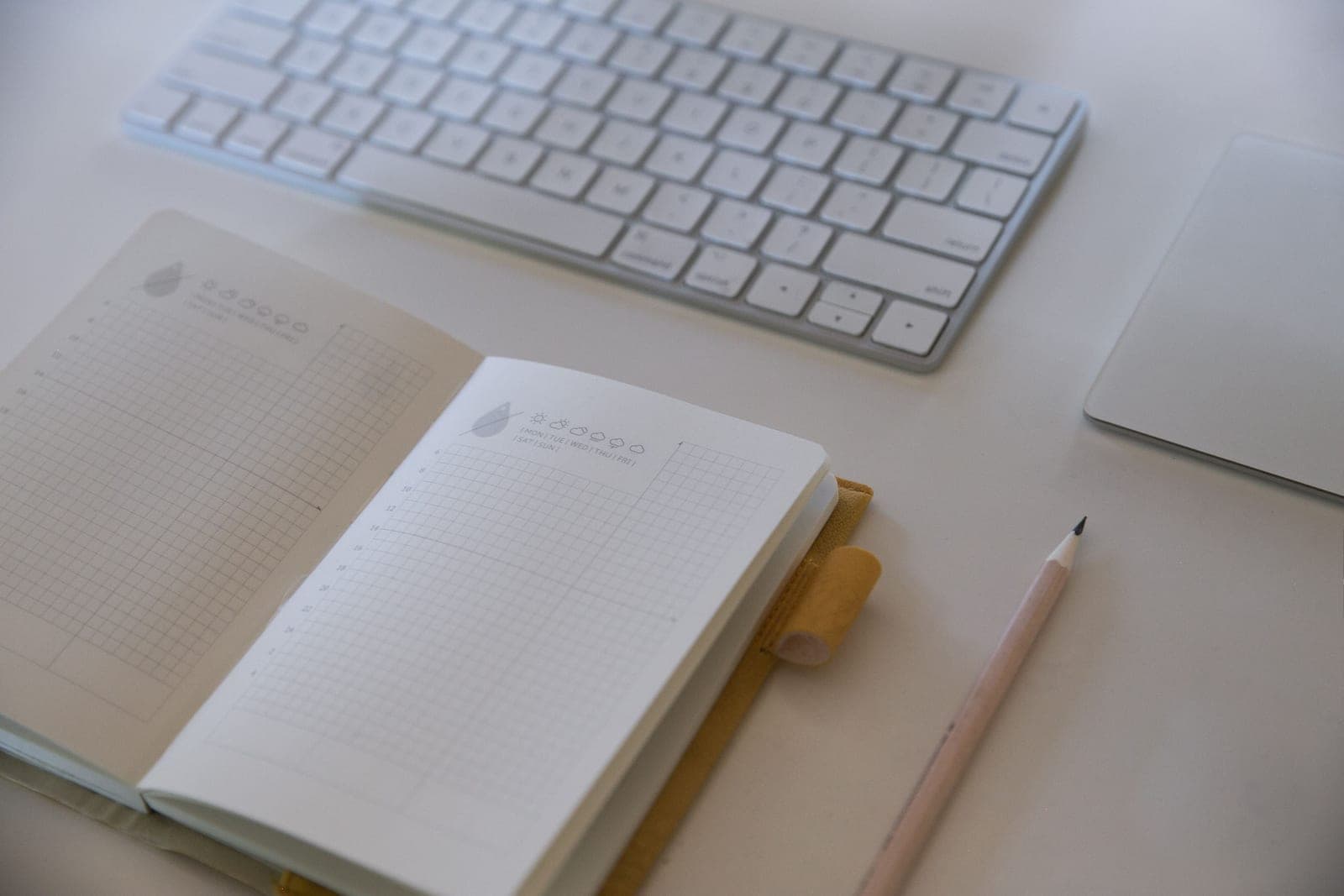 A tidy warm home office desk with a desk pad, keyboard and notebook