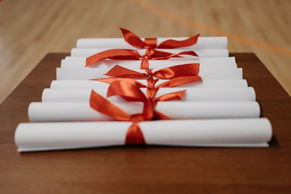 Rolled diplomas tied with ribbon resting on a wooden desk