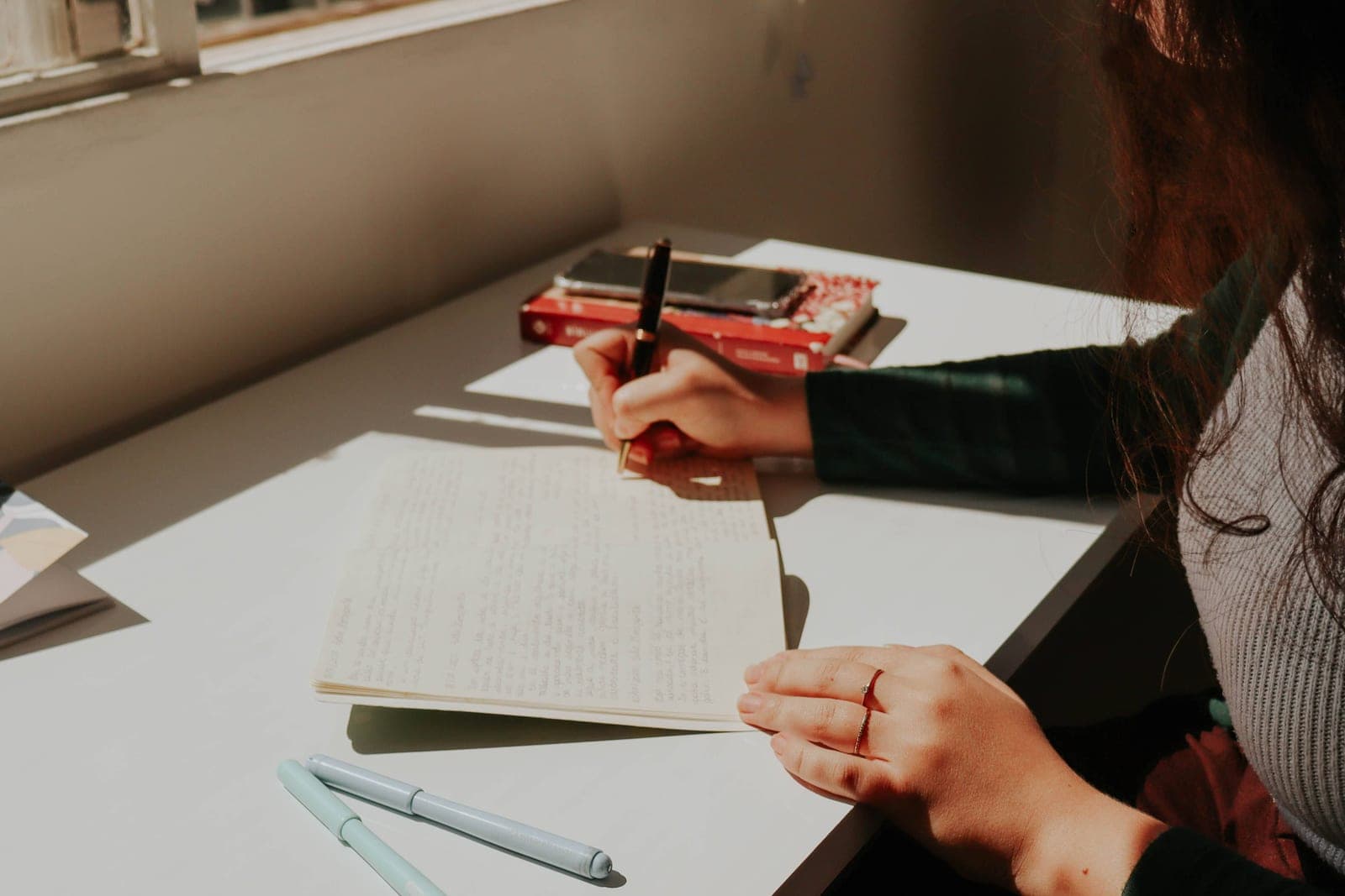 A woman writing in a notebook at a desk in warm daylight