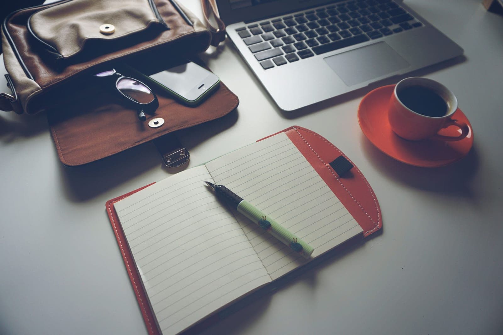 A leather desk pad, notebook and pen laid out on a wooden desk