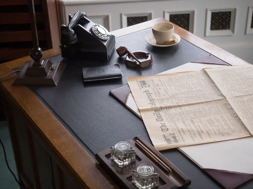 A vintage office desk with a leather blotter, inkwells, a pen and a rotary telephone