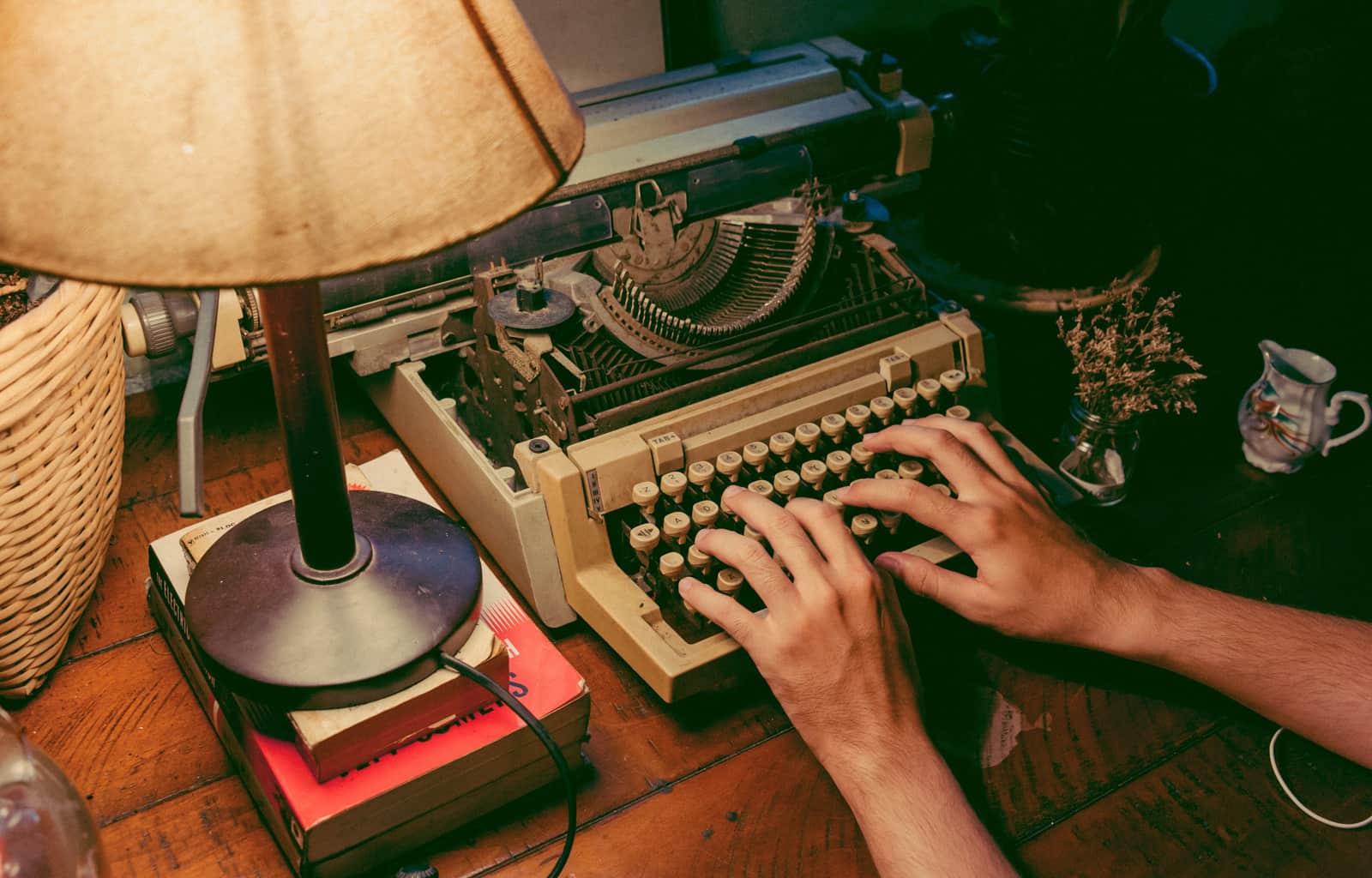 Hands writing in an open journal on a warm wooden desk