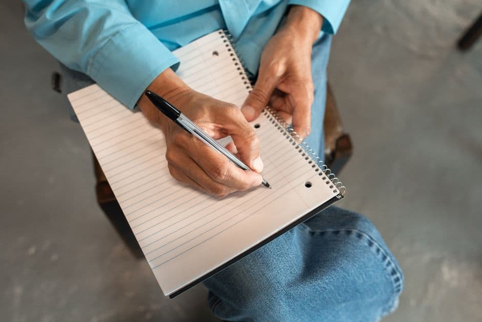 Close-up of hands writing in a spiral notebook with a pen