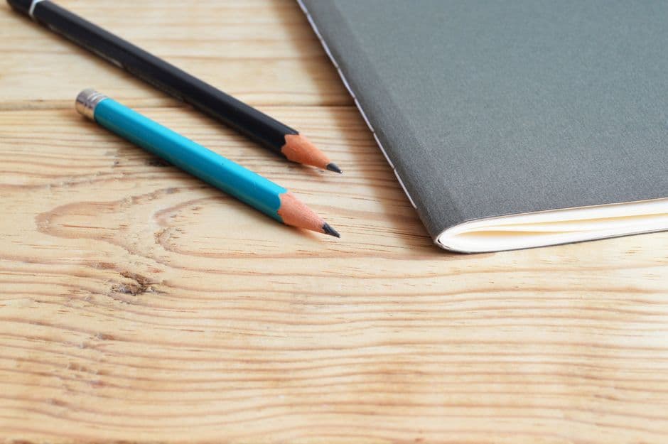 A notebook and pencils arranged on a wooden desk