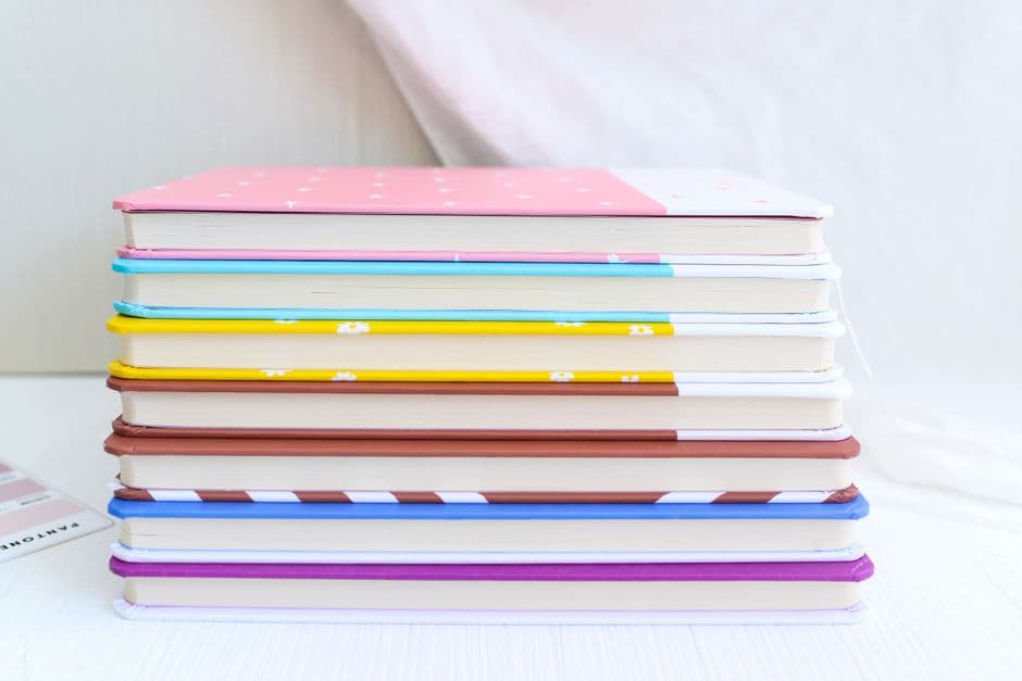 A stack of hardcover notebooks with colored covers on a plain surface