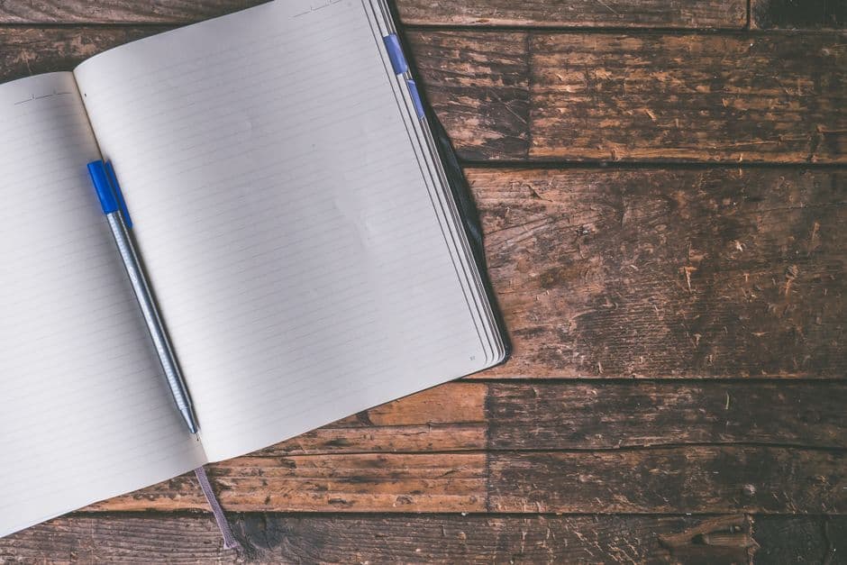 An open notebook lying flat on a rustic wooden table with a pen