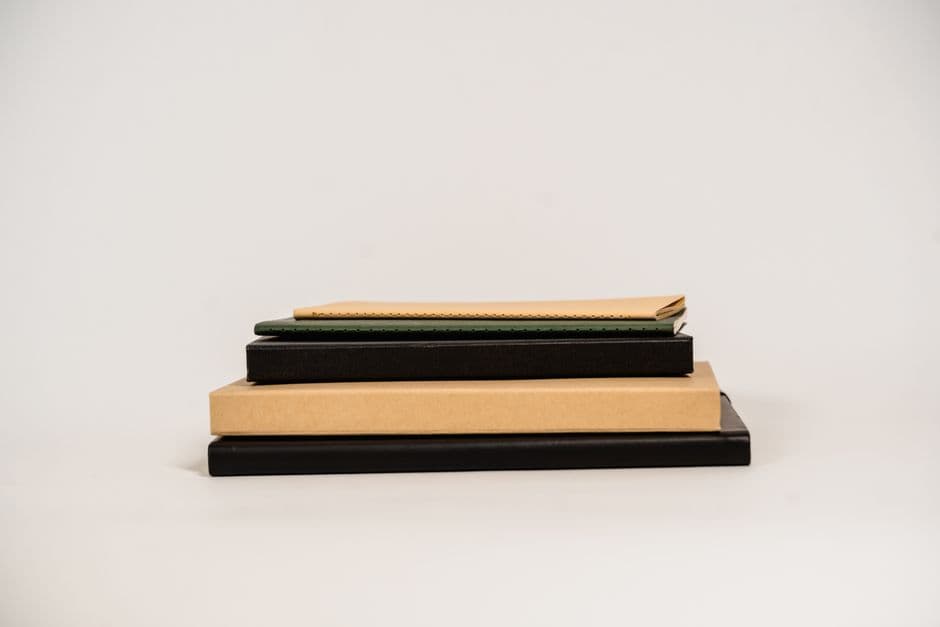 A stack of notebooks and books with assorted covers and bindings