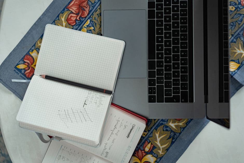 A flat lay of notebooks and a pencil on a patterned tablecloth