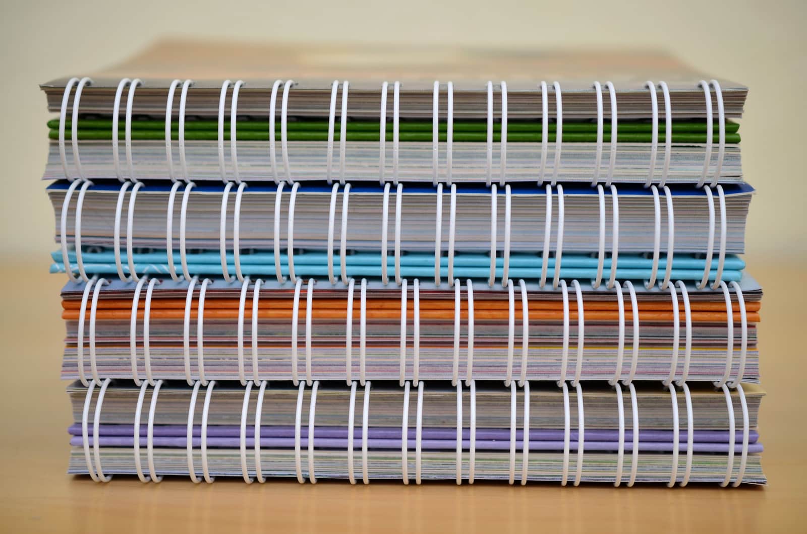A stack of assorted notebooks including spiral and hardcover on a wooden desk