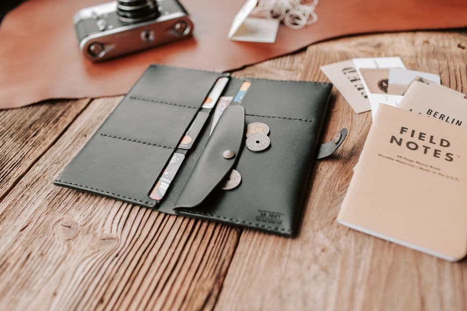 A leather wallet, coins and a small notebook on a wooden surface