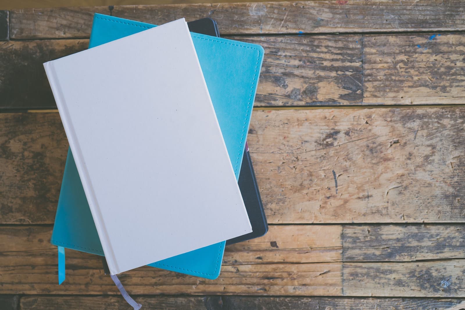 A stack of hardcover notebooks and journals on a warm wooden table