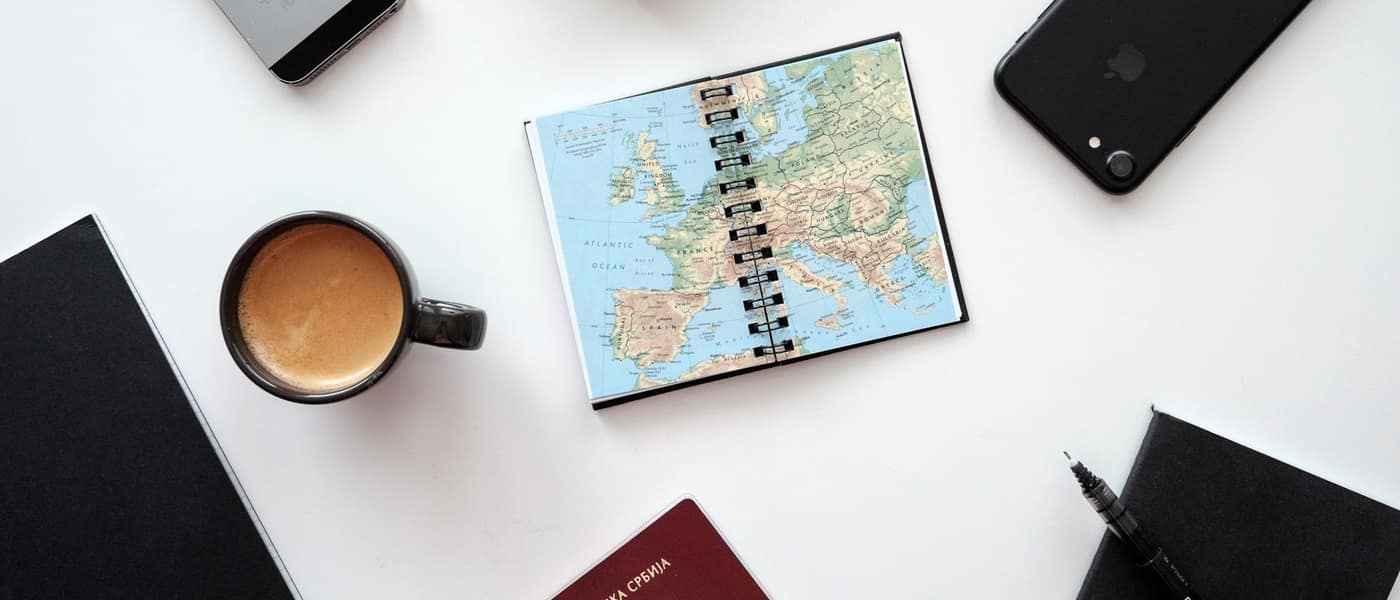 A map, passport, notebooks and a pen arranged on a white surface