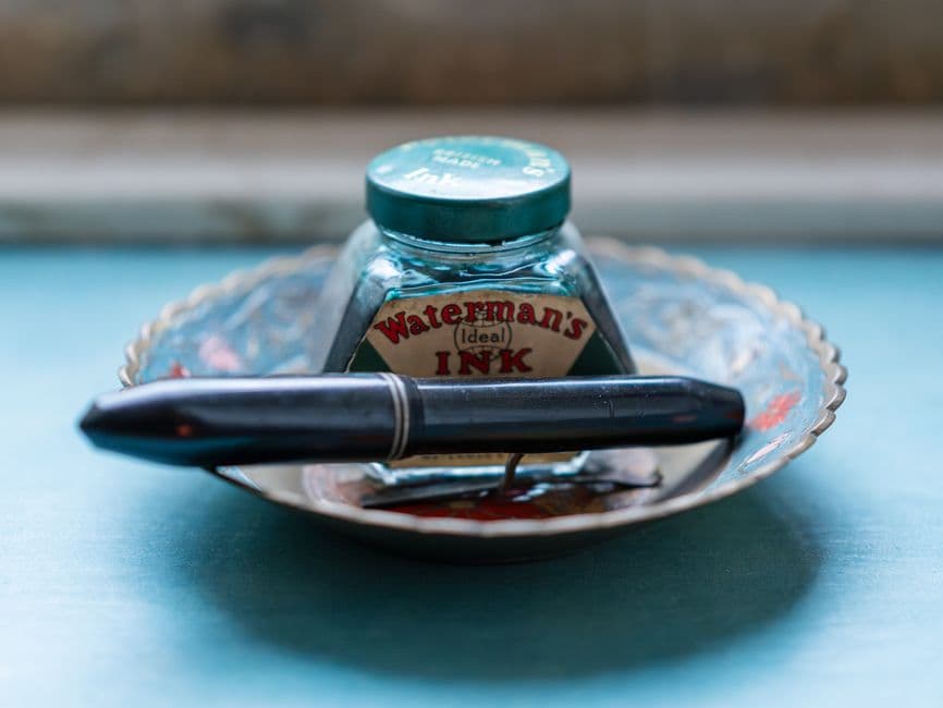 A vintage ink bottle and a pen resting on a small dish