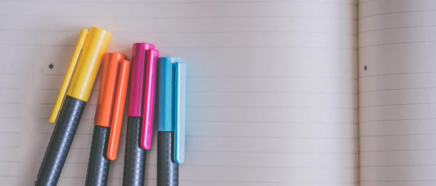 A collection of gel pens resting on an open lined notebook