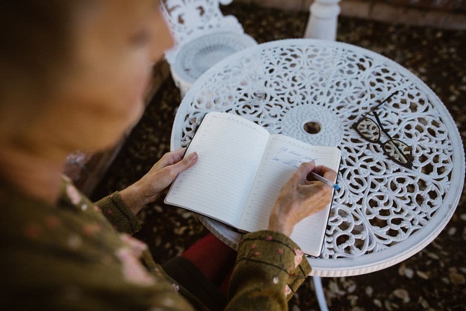 An older person writing in a notebook at an outdoor table