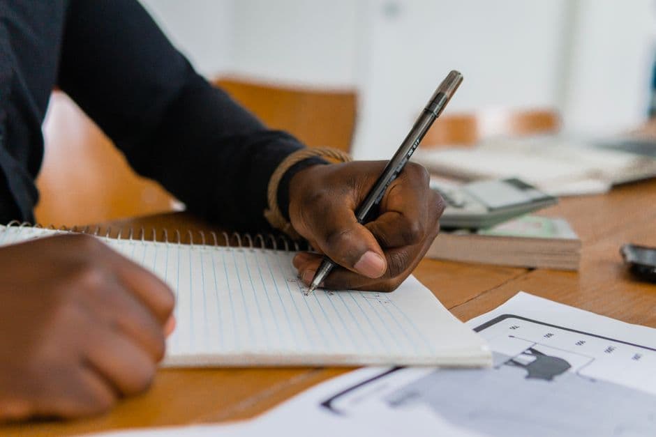 A close-up of a hand writing in a notebook on a wooden table