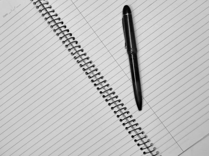 A pen resting on the lined page of an open spiral notebook