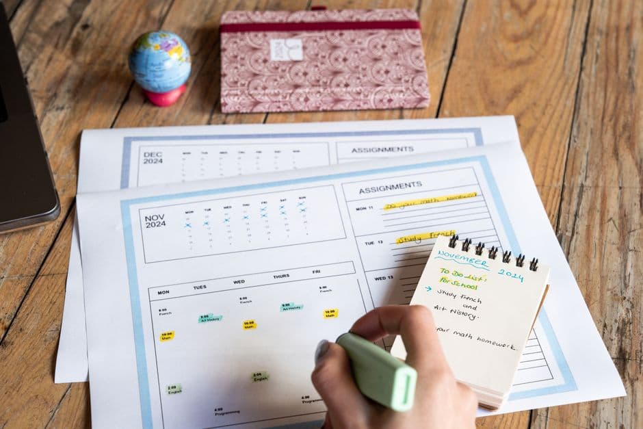 A person planning tasks with a calendar and notepad on a wooden table