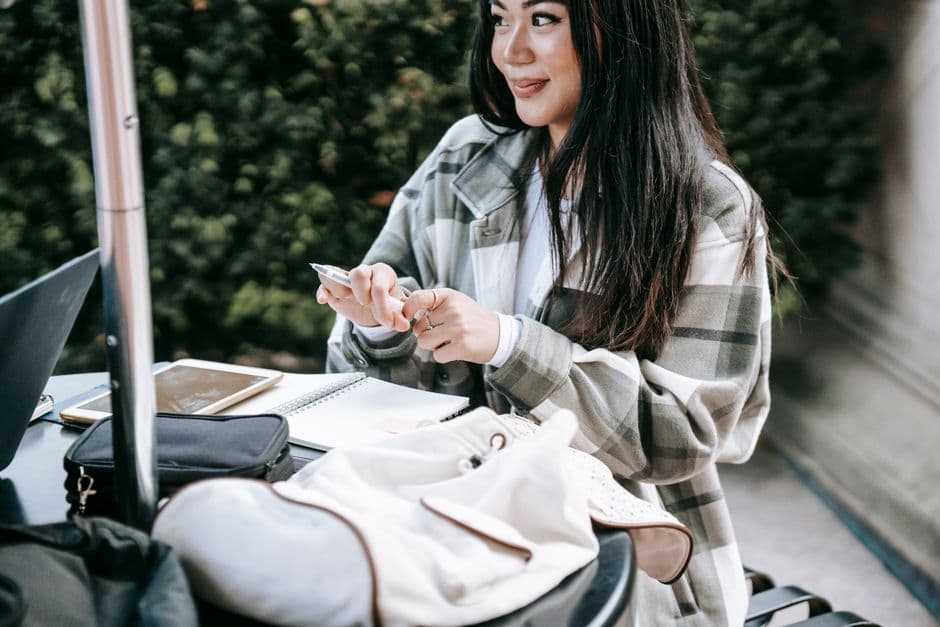 A student sitting at a table on campus writing notes in a notebook