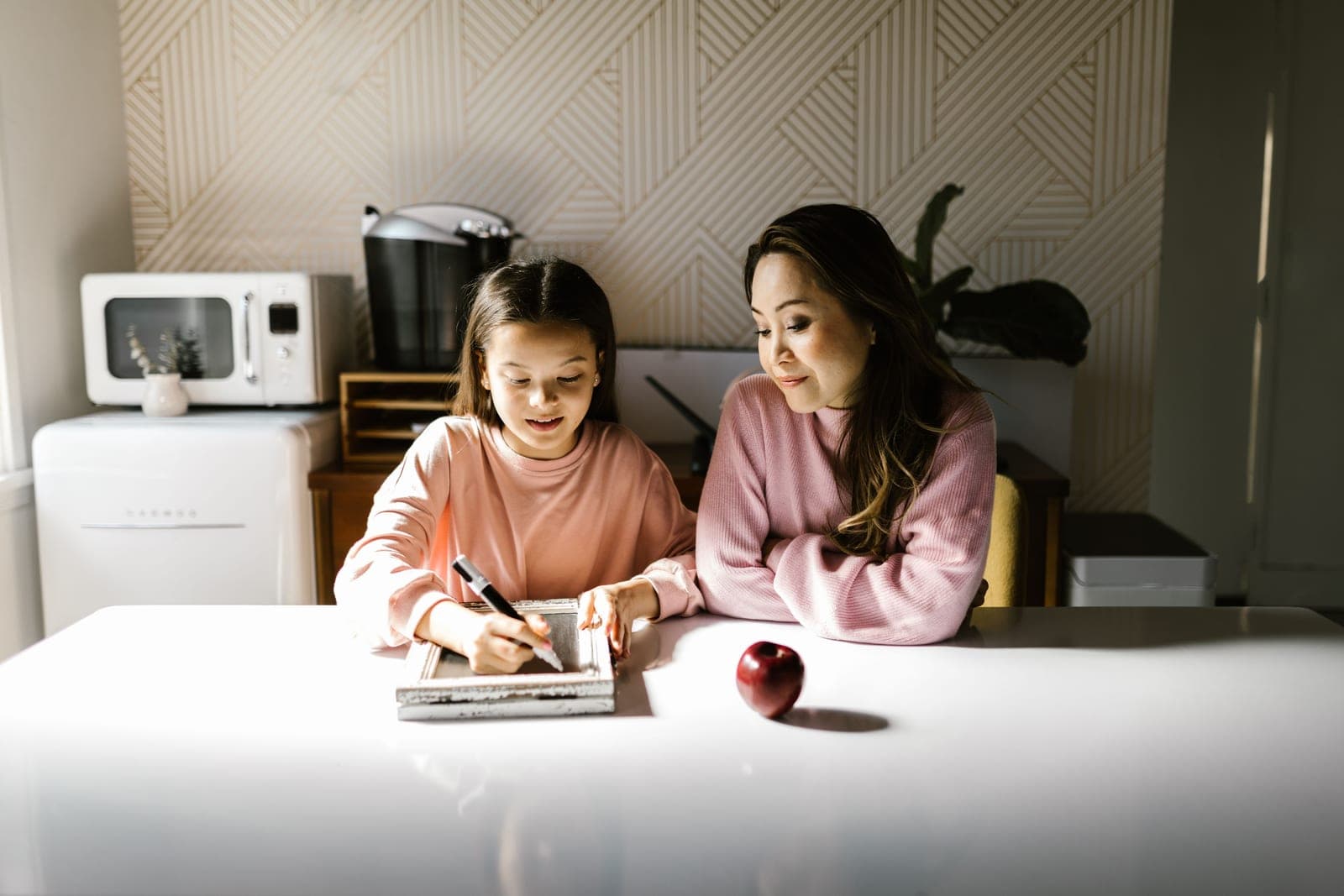 A parent writing on a family calendar in a kitchen in warm daylight