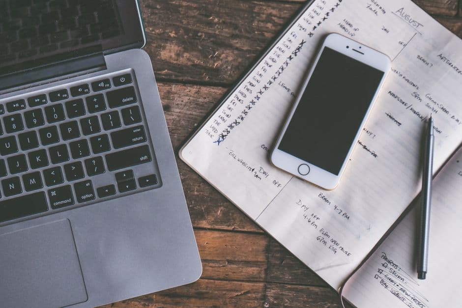 A desk from above with a laptop, a smartphone and an open notebook