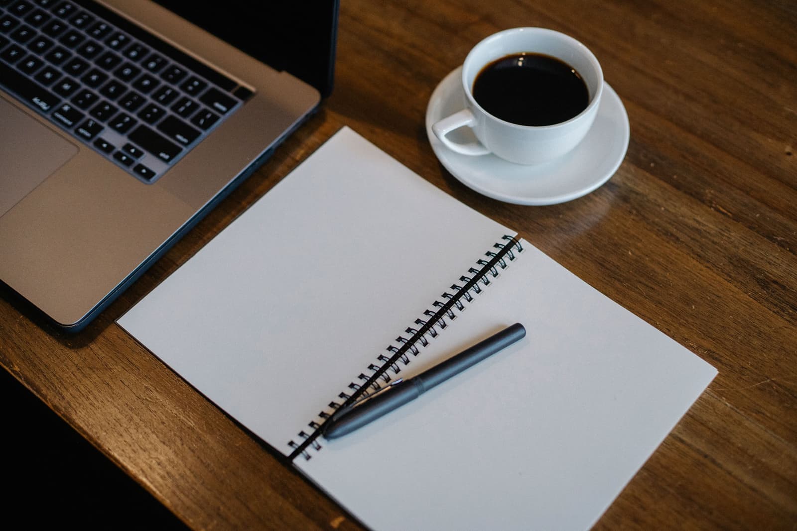 An open planner on an office desk beside a coffee cup and a laptop